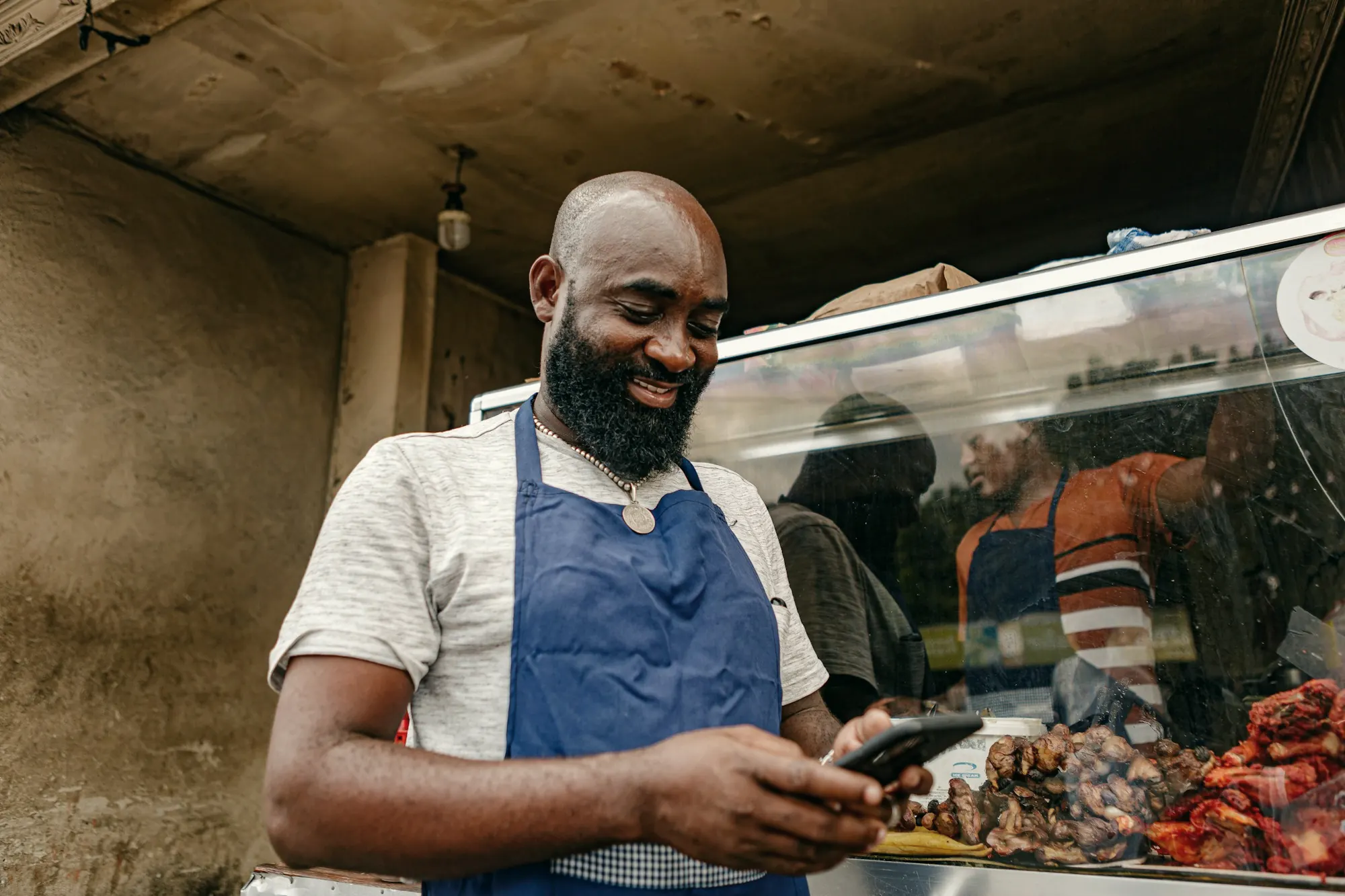 A shop owner checking orders on his phone behind the counter